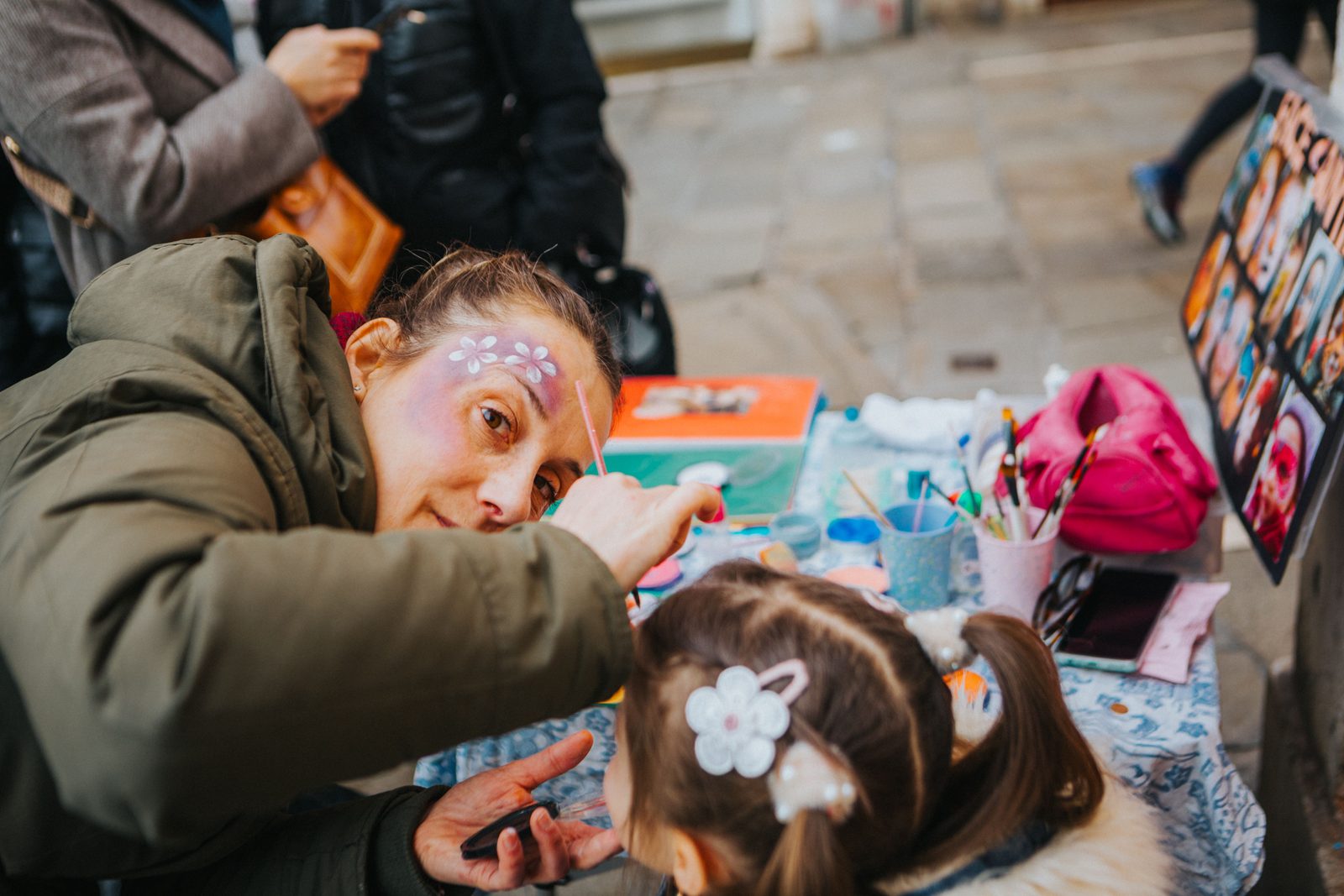 A face painter carefully decorating a child's face at an outdoor event