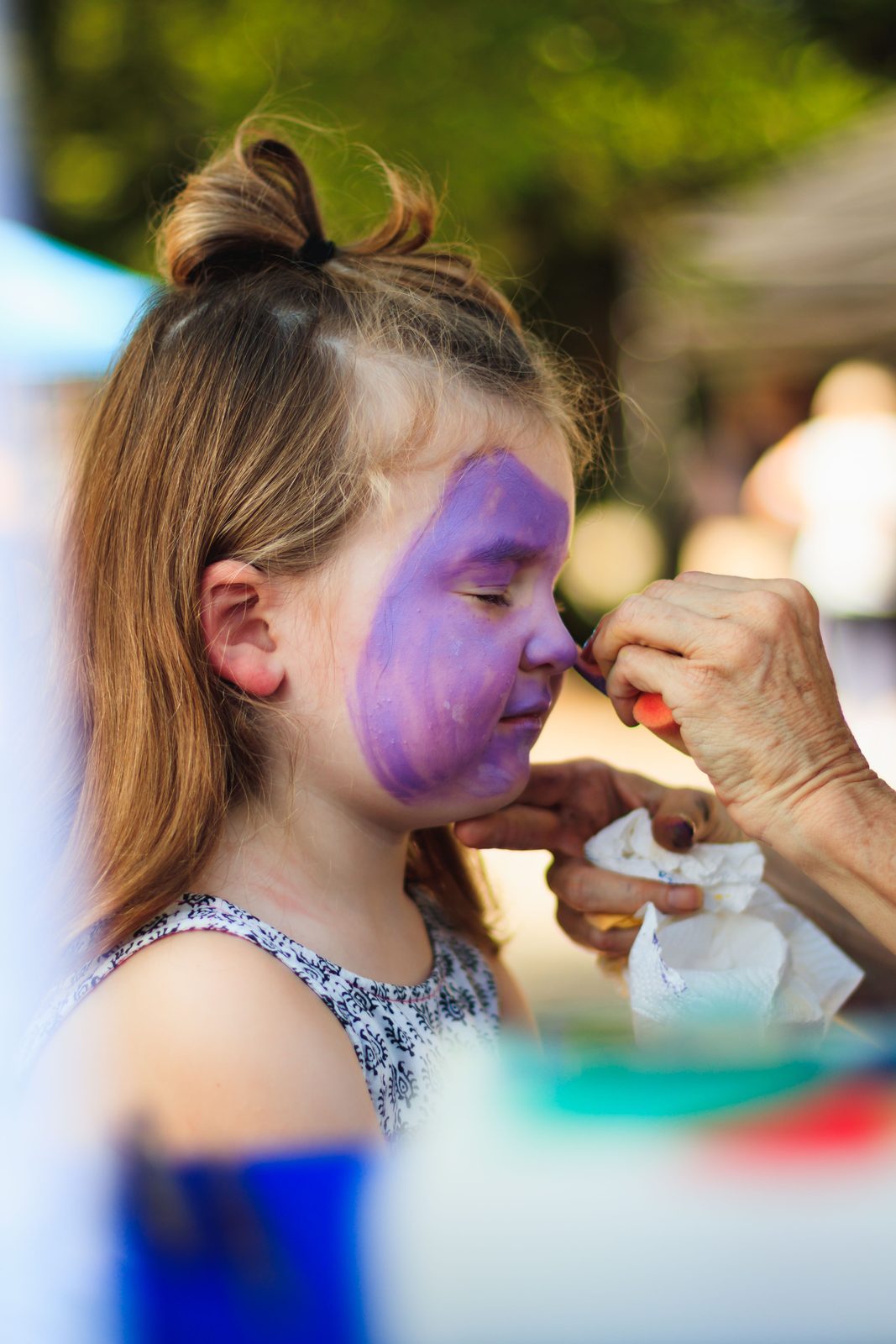 Young girl having her face painted purple